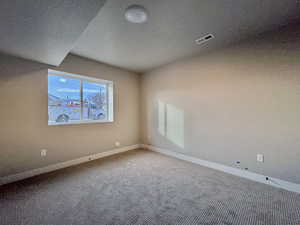 Carpeted spare room with a textured ceiling and a textured wall
