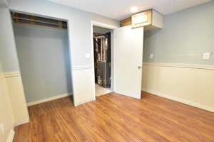 Unfurnished bedroom featuring a wainscoted wall, light wood-type flooring, a closet, a decorative wall, and heating unit