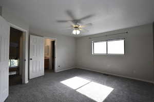 Unfurnished bedroom featuring dark colored carpet, ensuite bath, and ceiling fan