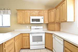 Kitchen with white appliances, light countertops, vaulted ceiling, light brown cabinetry, and light tile patterned floors