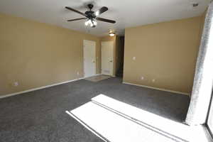 Carpeted spare room featuring ceiling fan and stairway