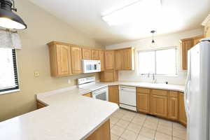 Kitchen featuring pendant lighting, white appliances, light countertops, lofted ceiling, and decorative backsplash