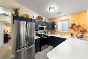 Kitchen featuring appliances with stainless steel finishes, light countertops, a textured ceiling, wallpapered walls, and vaulted ceiling