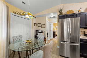 Dining space featuring lofted ceiling, wallpapered walls, and light wood-type flooring