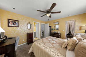 Bedroom with ensuite bath, dark colored carpet, ceiling fan, a textured ceiling, and a desk