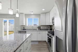 Kitchen featuring appliances with stainless steel finishes, white cabinets, pendant lighting, recessed lighting, and light stone countertops