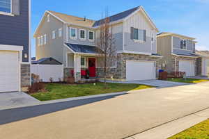 View of front of property with stone siding, board and batten siding, a front lawn, an attached garage, and driveway