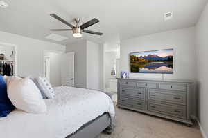 Bedroom featuring light colored carpet, connected bathroom, a ceiling fan, and a spacious closet