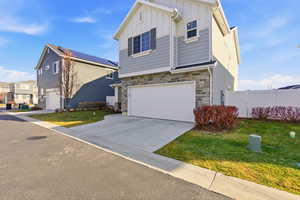View of front facade with board and batten siding, stone siding, driveway, and an attached garage