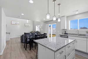 Kitchen featuring open floor plan, light stone counters, hanging light fixtures, white cabinets, and light wood-style floors