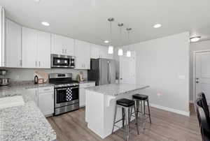 Kitchen with a kitchen bar, appliances with stainless steel finishes, pendant lighting, a center island, and white cabinetry