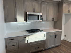 Kitchen featuring light stone countertops, appliances with stainless steel finishes, tasteful backsplash, and dark wood-style floors