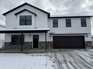 View of front of house featuring an attached garage, a porch, stone siding, and driveway