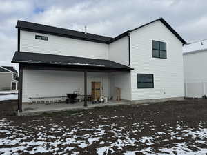 Snow covered back of property featuring a patio area and roof with shingles