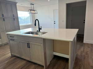 Kitchen with dark wood finished floors, pendant lighting, a kitchen island with sink, light stone countertops, and recessed lighting