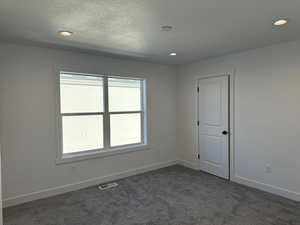 Spare room featuring dark colored carpet, recessed lighting, and a textured ceiling