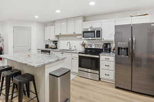 Kitchen with stainless steel appliances, a center island, light stone counters, recessed lighting, and white cabinets