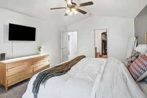 Bedroom with vaulted ceiling, dark carpet, a ceiling fan, and connected bathroom