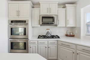 Kitchen featuring appliances with stainless steel finishes, tasteful backsplash, white cabinets, and light stone counters