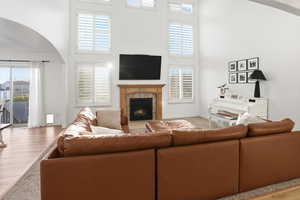 Living room featuring arched walkways, a towering ceiling, a brick fireplace, plenty of natural light, and wood finished floors