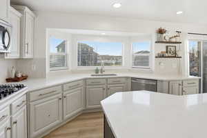 Kitchen featuring white cabinets, backsplash, appliances with stainless steel finishes, light stone counters, and plenty of natural light