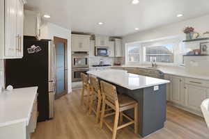Kitchen with appliances with stainless steel finishes, a kitchen bar, a center island, open shelves, and light wood-style floors