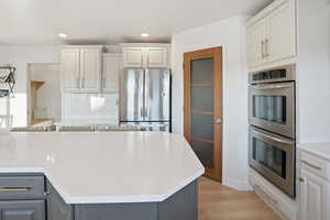 Kitchen featuring appliances with stainless steel finishes, tasteful backsplash, white cabinetry, light stone counters, and light wood-style floors