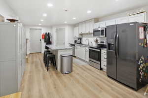 Kitchen featuring stainless steel appliances, a kitchen bar, a center island, light stone counters, and recessed lighting