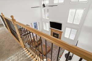 Stairway with a lit fireplace, a high ceiling, carpet, healthy amount of natural light, and ceiling fan