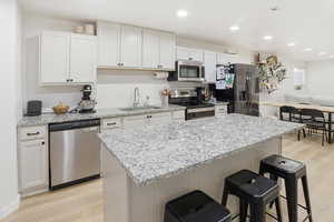 Kitchen featuring a kitchen breakfast bar, appliances with stainless steel finishes, recessed lighting, white cabinets, and light stone countertops