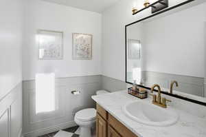 Bathroom featuring wainscoting, vanity, a decorative wall, and dark floors