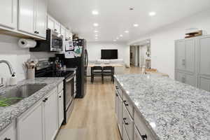 Kitchen with open floor plan, appliances with stainless steel finishes, light wood-style floors, light stone counters, and recessed lighting