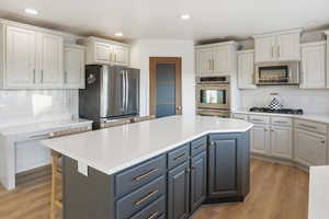 Kitchen with decorative backsplash, a center island, stainless steel appliances, light stone countertops, and recessed lighting