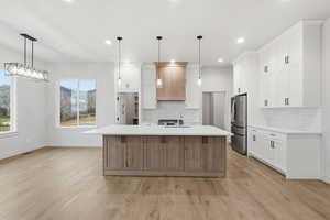 Kitchen featuring hanging light fixtures, a kitchen island with sink, white cabinets, light wood-type flooring, and recessed lighting