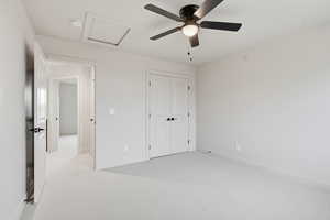 Unfurnished bedroom with attic access, light carpet, a ceiling fan, and a closet