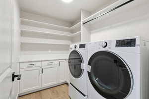 Laundry area featuring light wood-style flooring, washer and dryer, and cabinet space