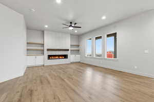 Unfurnished living room with recessed lighting, a fireplace, light wood-type flooring, a ceiling fan, and built in shelves