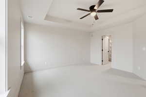 Spare room featuring a raised ceiling, carpet floors, and ceiling fan