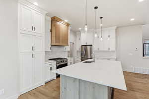 Kitchen featuring a center island with sink, appliances with stainless steel finishes, decorative light fixtures, white cabinetry, and recessed lighting