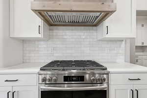 Kitchen with range hood, stainless steel gas range oven, white cabinets, and decorative backsplash