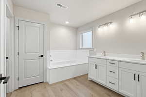 Full bath featuring double vanity, a garden tub, light wood-style floors, and recessed lighting