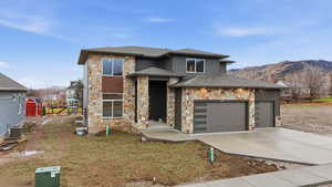 Prairie-style house with stone siding, concrete driveway, a shingled roof, an attached garage, and a mountain view