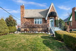Tudor-style house with a tile roof, brick siding, a front lawn, and a chimney