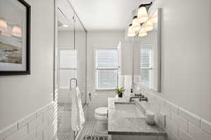 Bathroom with tile walls, a wainscoted wall, vanity, a stall shower, and light tile patterned flooring