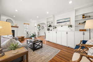 Living room with arched walkways, built in shelves, a glass covered fireplace, light wood-style flooring, and recessed lighting