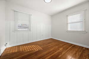 Unfurnished room featuring hardwood / wood-style floors, wainscoting, and a decorative wall