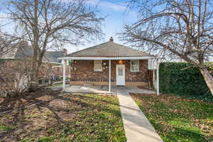 Bungalow with brick siding, a chimney, covered porch, and a tile roof
