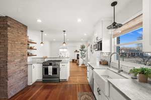 Kitchen featuring white cabinets, hanging light fixtures, stainless steel appliances, light stone counters, and recessed lighting