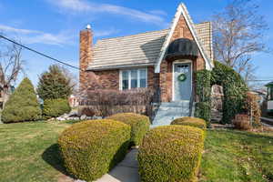 English style home with a front yard, a tiled roof, brick siding, and a chimney