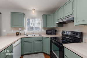 Kitchen with green cabinetry, black appliances, light countertops, and under cabinet range hood